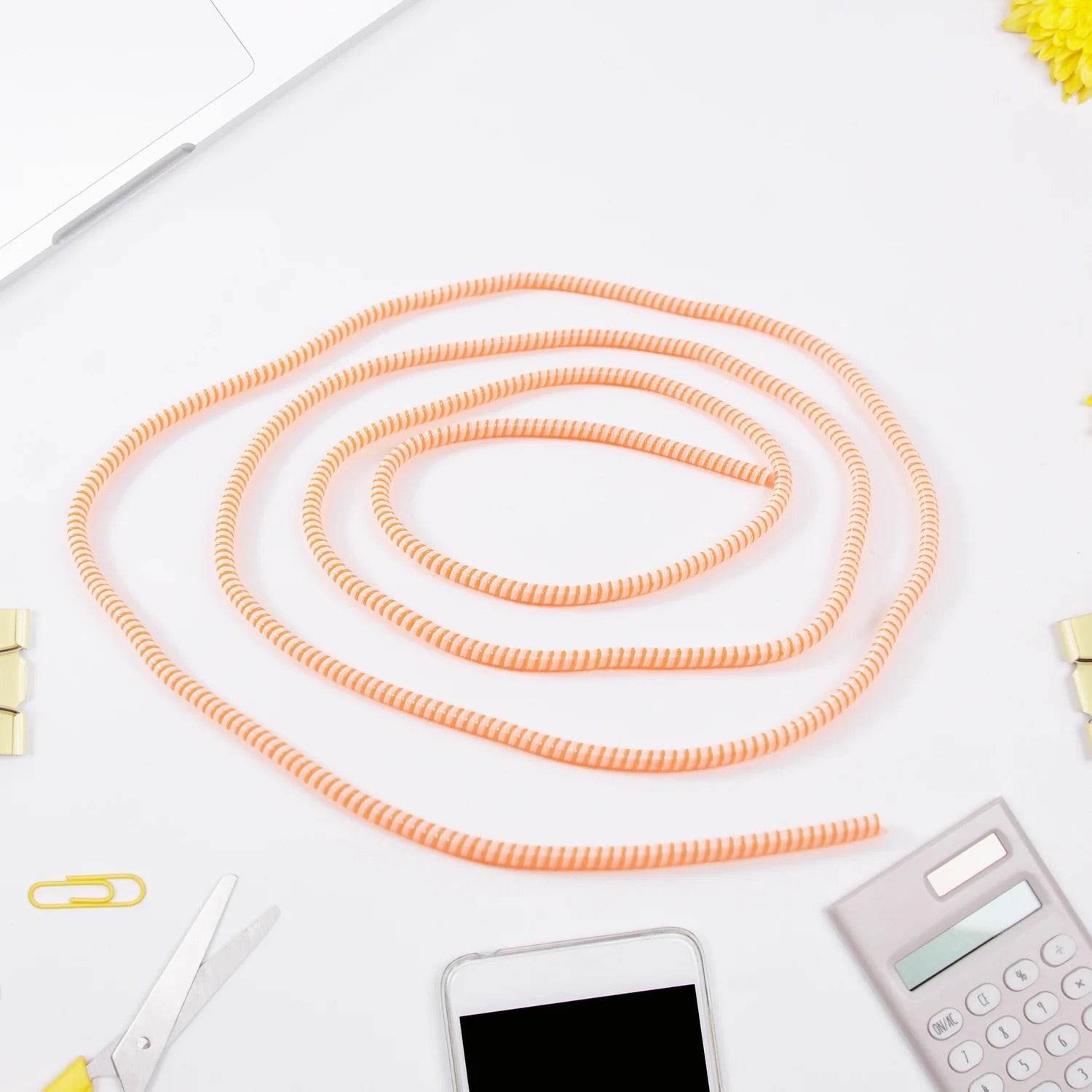 Orange spiral cable protector sleeve coiled on desk near phone, calculator, scissors, and laptop