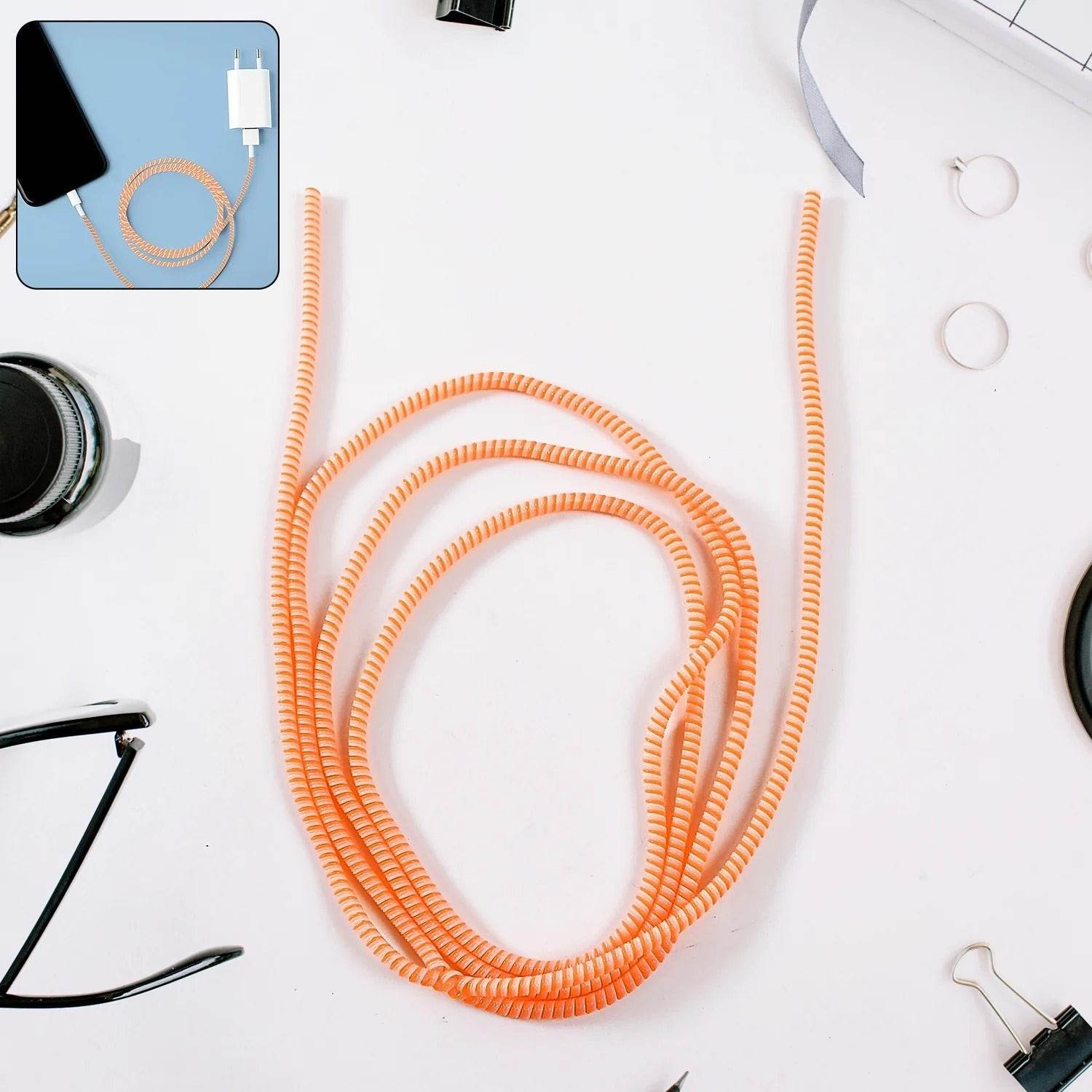Orange spiral cable protector sleeve coiled on white background with office accessories around
