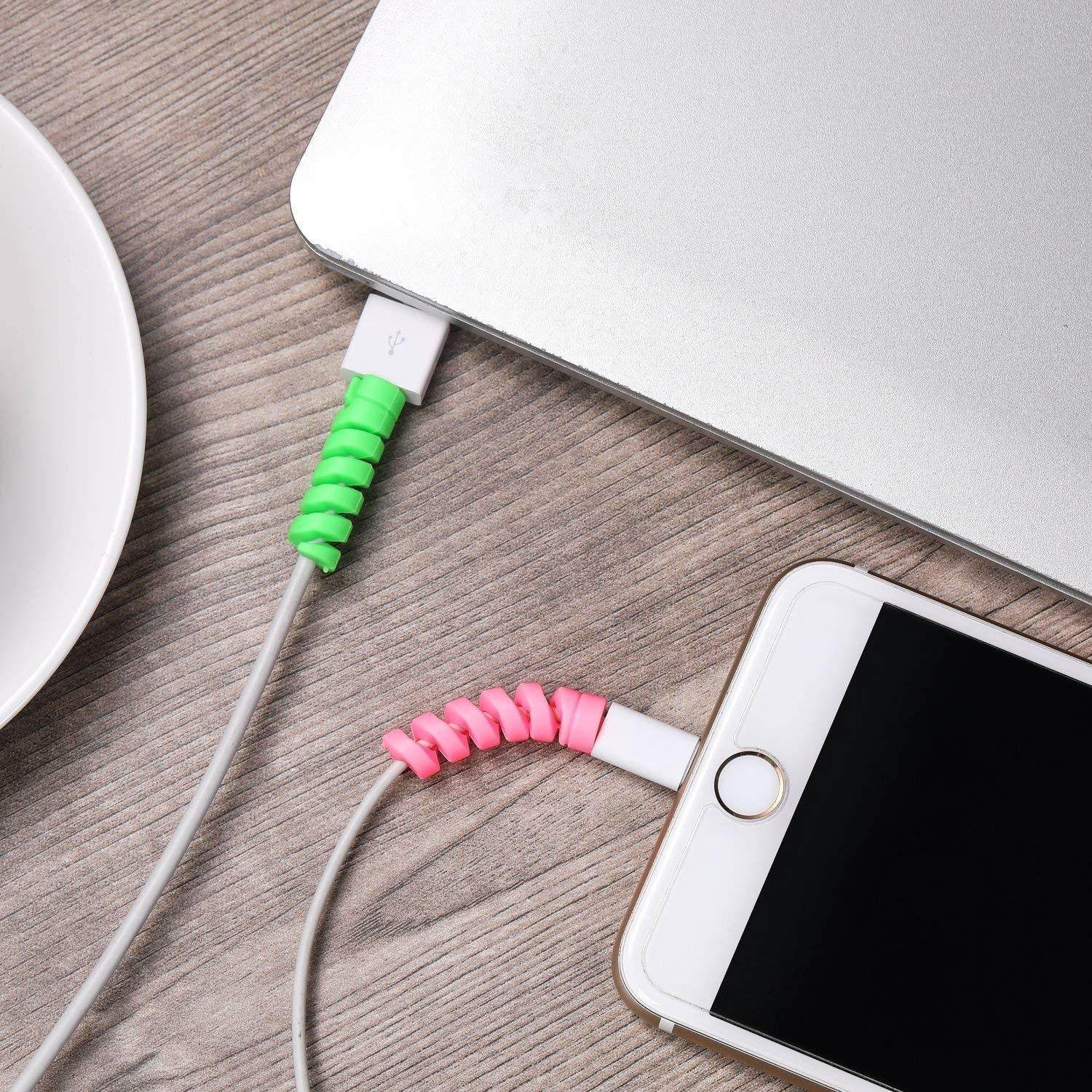Green and pink spiral cable protectors on charging cables connected to laptop and smartphone